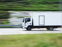 White moving truck driving quickly on a highway, transporting fitness equipment